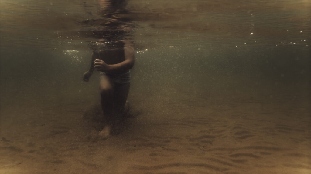 Vue sous-marine d'un enfant marchant dans l'eau, silhouette baignée de lumière dorée