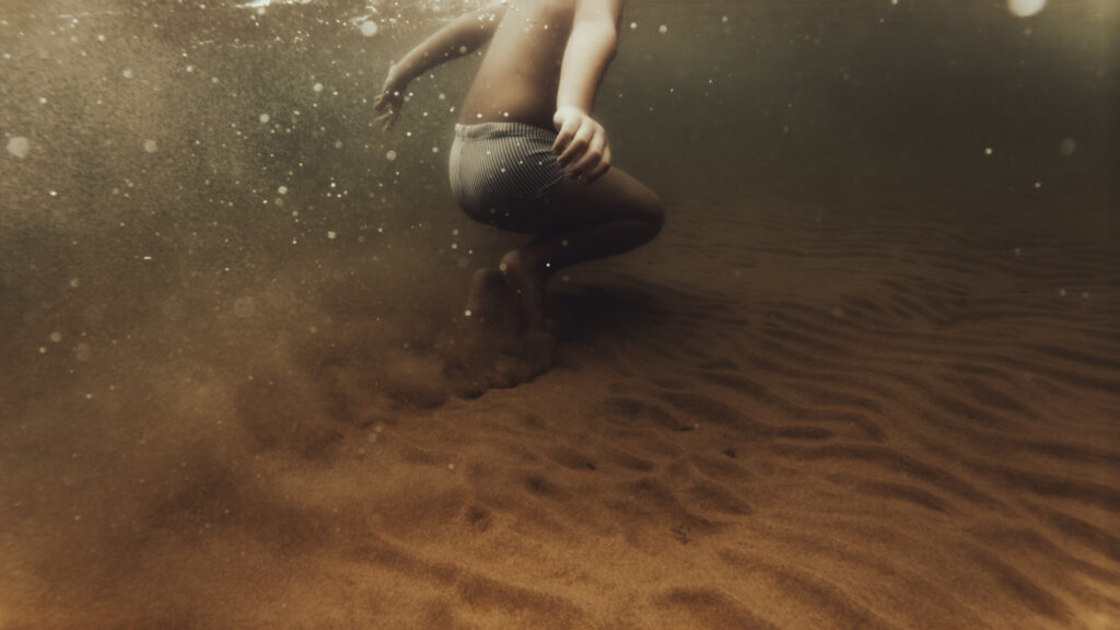 Vue sous-marine d'un enfant en maillot de bain rayé marchant sur un fond de sable.