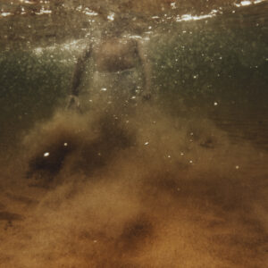 Vue sous-marine d'une personne partiellement visible dans une eau trouble et ambrée, avec du sable en suspension.