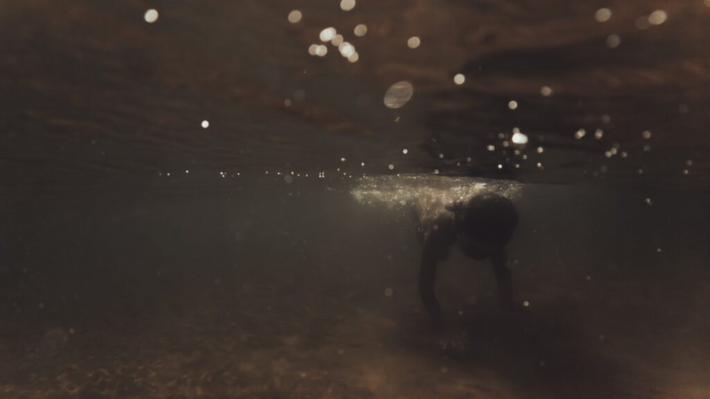 Silhouette d'une personne vue sous l'eau, entourée de bulles et de lumière filtrante.
