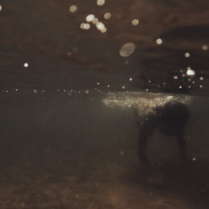 Silhouette d'une personne vue sous l'eau, entourée de bulles et de lumière filtrante.