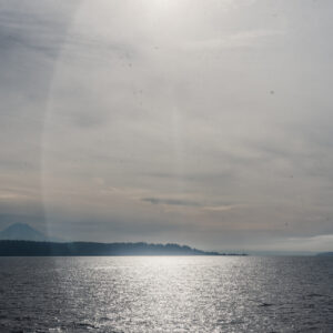 Vue sur une étendue d'eau scintillante avec une ligne côtière boisée et une montagne à l'horizon sous un ciel nuageux.