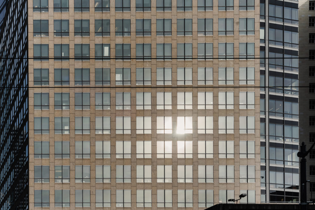Façade d'un immeuble de bureaux avec une grille régulière de fenêtres, dont une partie reflète intensément la lumière du soleil.