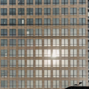 Façade d'un immeuble de bureaux avec une grille régulière de fenêtres, dont une partie reflète intensément la lumière du soleil.