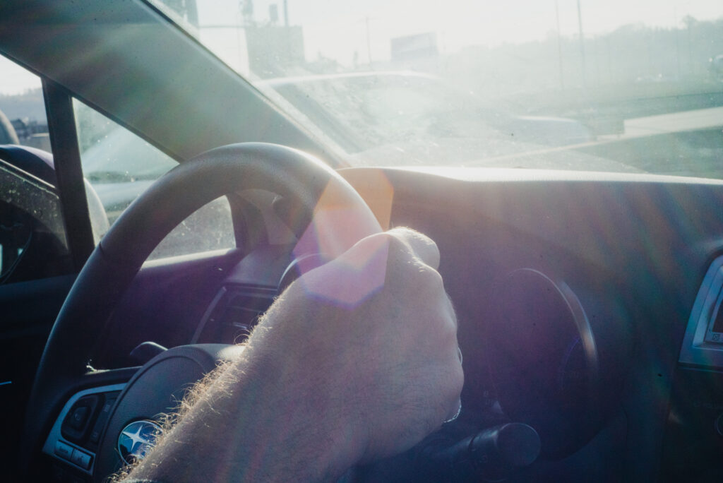 Une main tient le volant d'une voiture, baignée par la lumière du matin traversant le pare-brise.