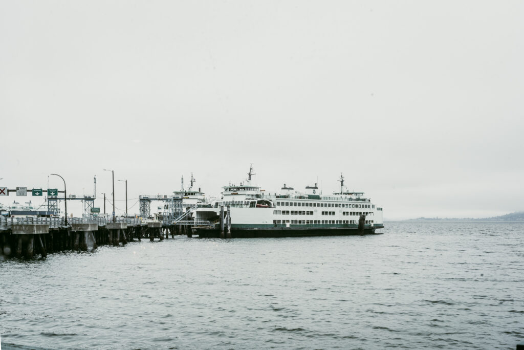 Un ferry blanc et vert amarré à un ponton en bois sous un ciel brumeux, avec des panneaux de signalisation à l'entrée du quai.