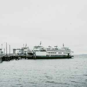 Un ferry blanc et vert amarré à un ponton en bois sous un ciel brumeux, avec des panneaux de signalisation à l'entrée du quai.