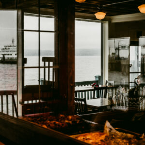 Une personne assise près d'une fenêtre de restaurant regarde un ferry naviguer sur une mer brumeuse.