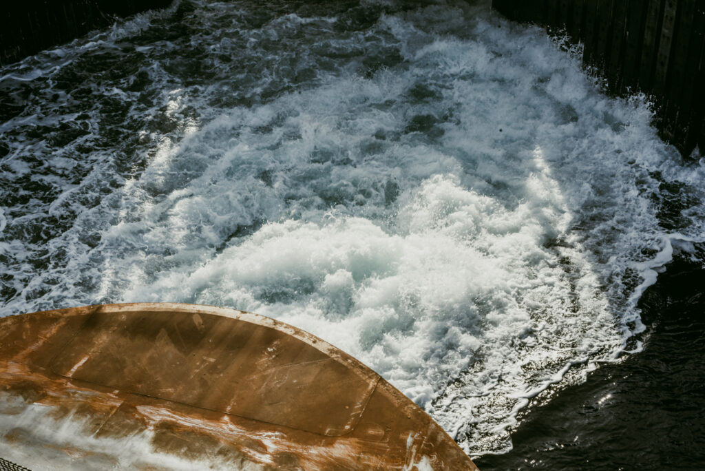 Vue plongeante sur l'arrière rouillé d'un bateau laissant un sillage d'écume blanche dans l'eau sombre.