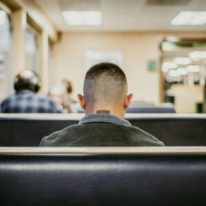 Un homme vu de dos, assis dans une cabine de transport, avec un tatouage en forme de code-barres sur la nuque.